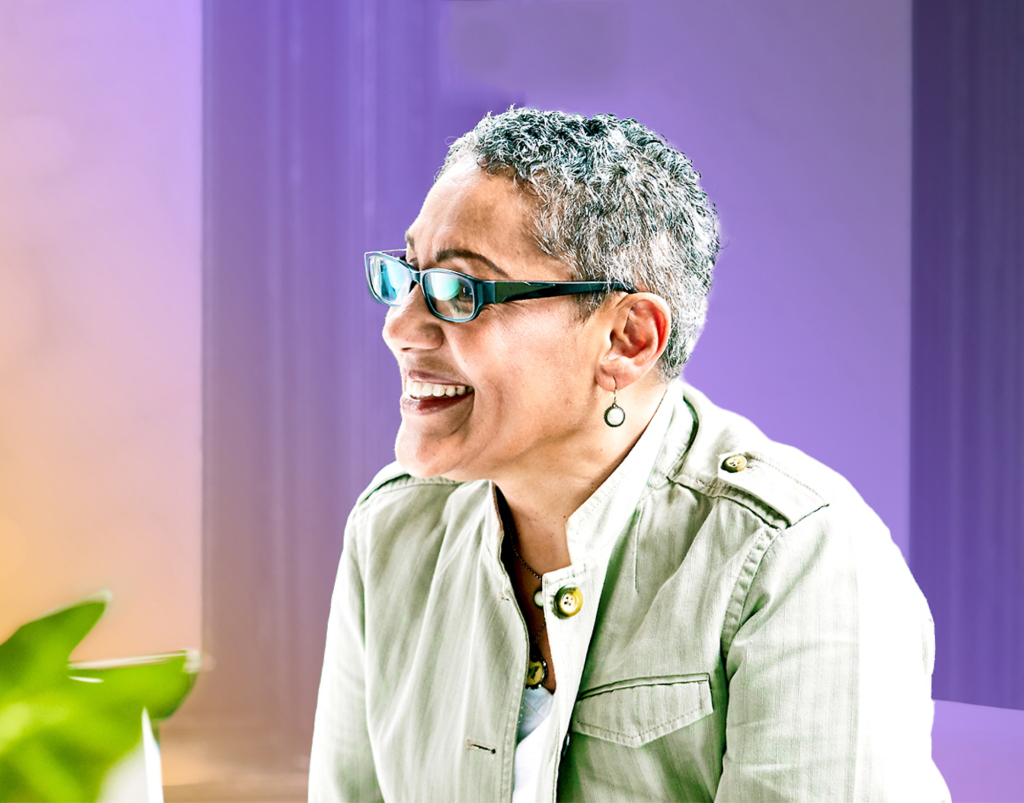 Usmívající se žena ve zralém věku s krátkými šedivými vlasy, v brýlích a světle zeleném saku
