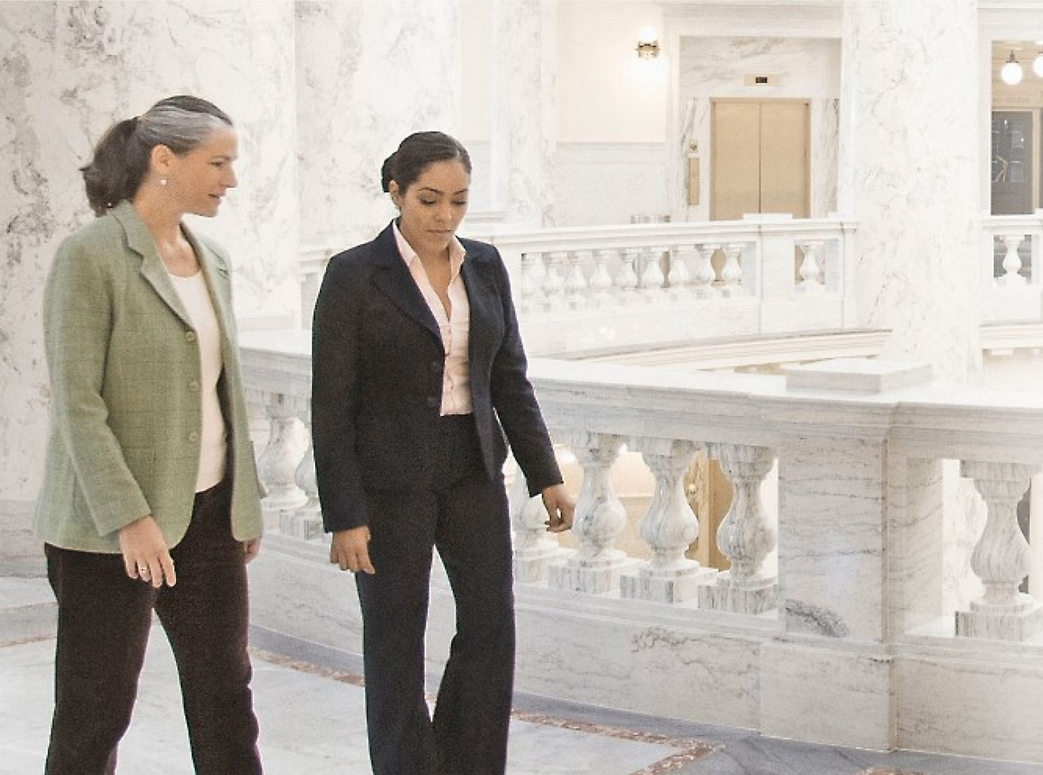 飾り付けられた手すりを背景にした大理石のホール内を歩きながら会話している 2 人の女性。