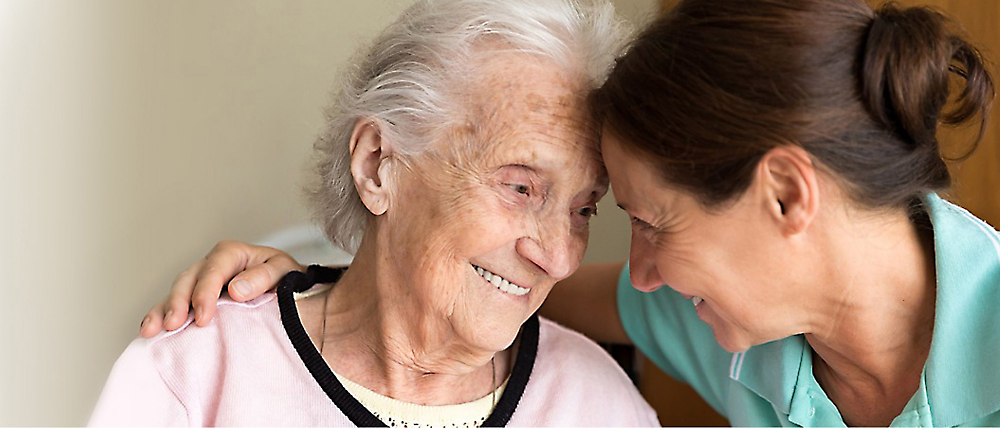 暖かい室内で、笑顔の年配の女性に対して親しみを込めて微笑んでいる介護人。