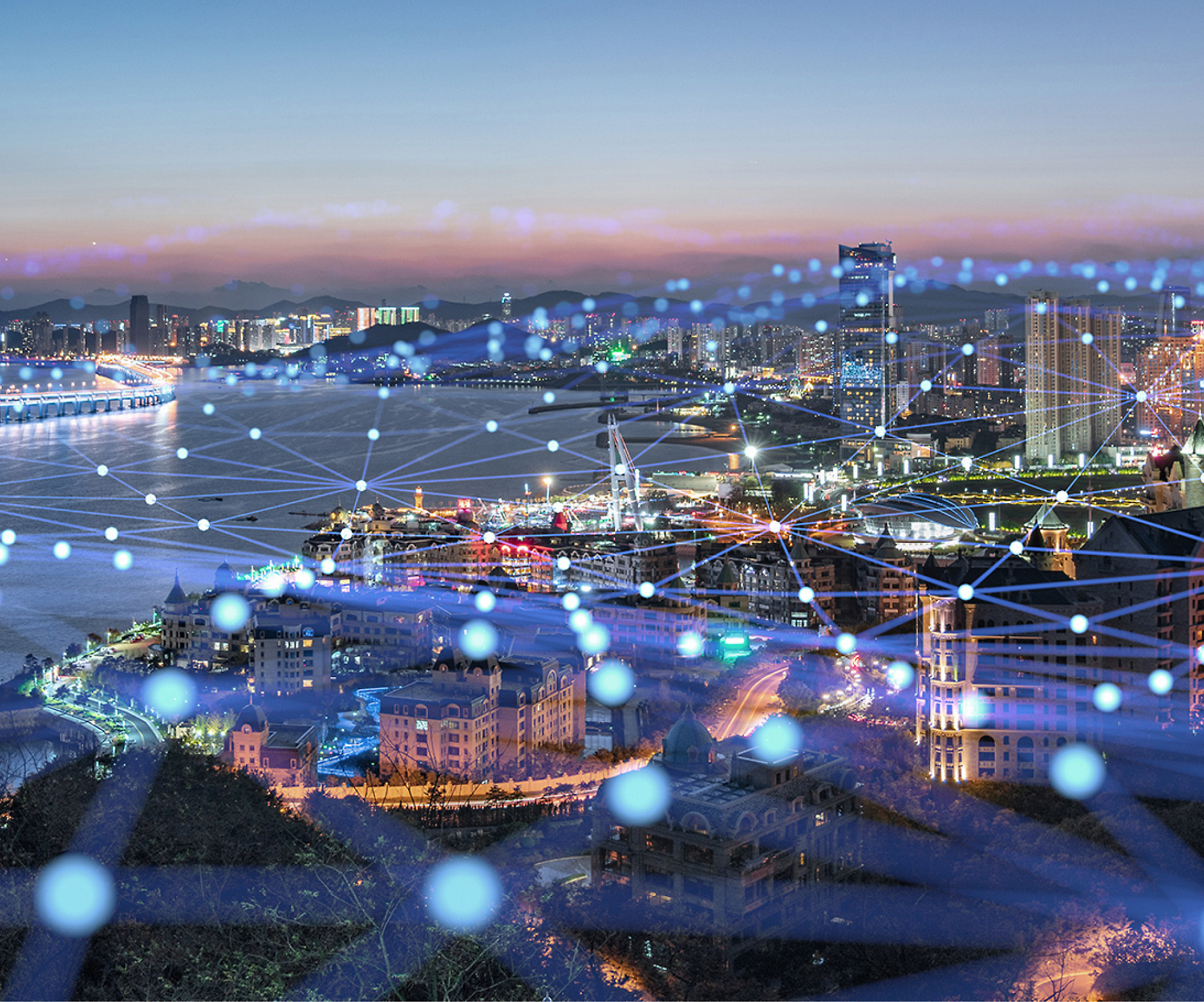 Letecký pohled na pobřežní město za soumraku s osvětlenými ulicemi a budovami, které překrývá zářící digitální síť