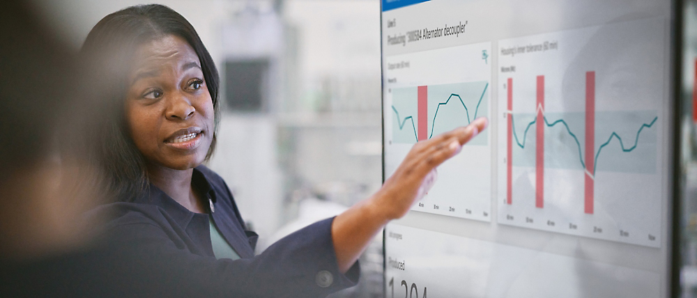 Profesionálně působící žena, která během schůzky prezentuje finanční údaje na digitální obrazovce a gestikuluje nad grafy a diagramy