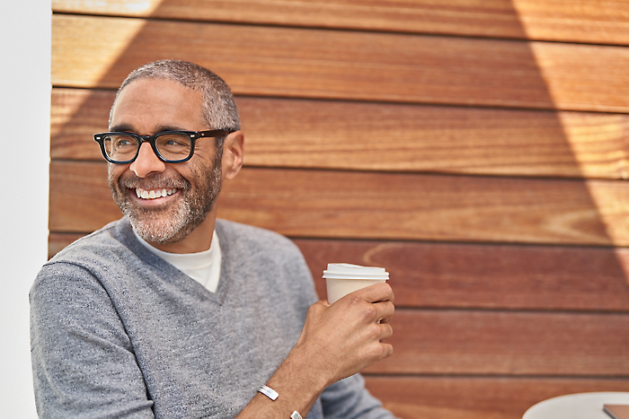 Una persona con gafas, sosteniendo una taza y sonriendo.