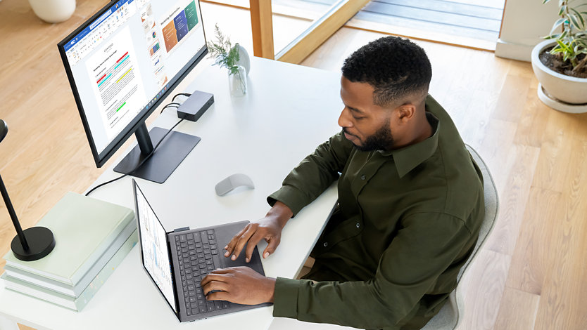En person använder Surface Laptop 5 för företag sittandes vid ett skrivbord på ett kontor. 