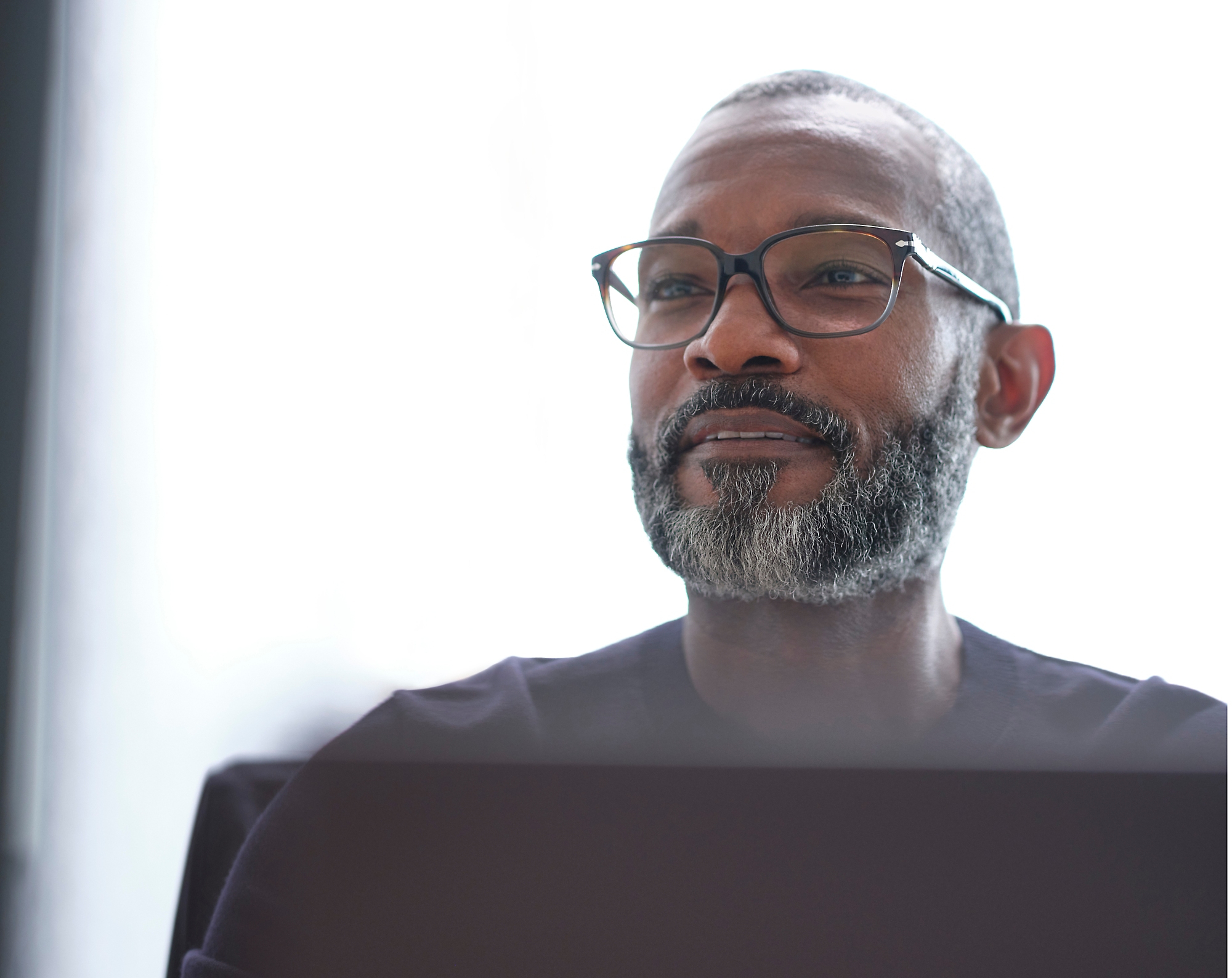 A man with glasses and a beard looking out over his laptop
