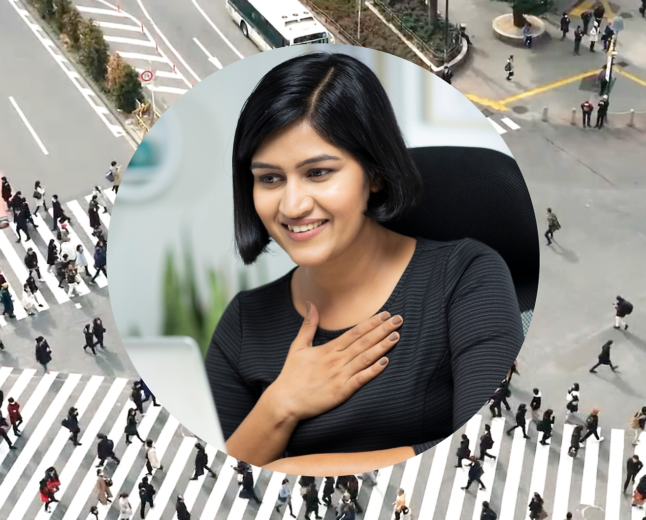 Egy nő, aki a kezét a mellkasához szorítja, miközben a laptopján dolgozik, a háttérképe egy útkereszteződés, amelyen emberek haladnak át