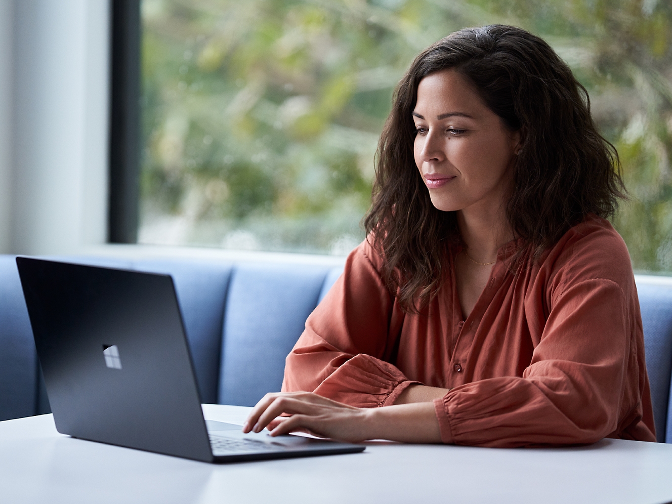 صورة لامرأة تجلس على طاولة وتستخدم جهاز كمبيوتر محمول.