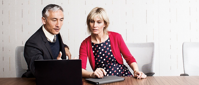 Egy férfi és egy nő egy asztalnál ülve egy laptopot néz.