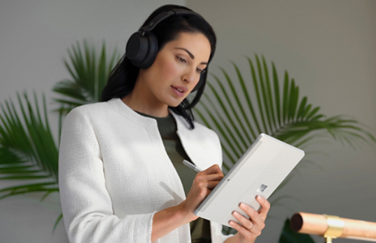 A person wearing Surface Headphones 2+ using Surface Pen to navigate Surface Go 4 in tablet mode at work.