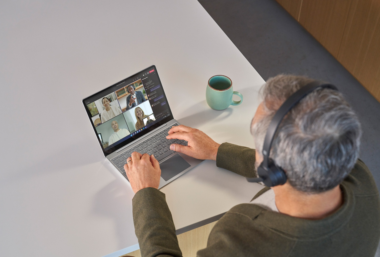 Bovenaanzicht van iemand met Surface Headphones 2 tijdens een Teams-vergadering op een Surface Laptop Go 3