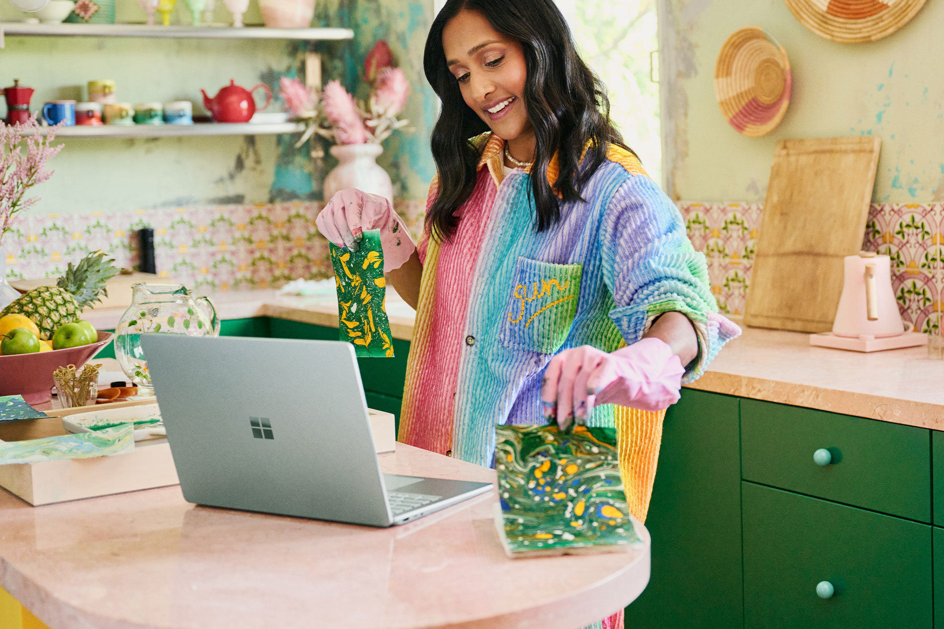 Une femme fait face à un comptoir. Elle tient des objets d’artisanat qu’elle a réalisés devant la caméra de son Surface Laptop 5.