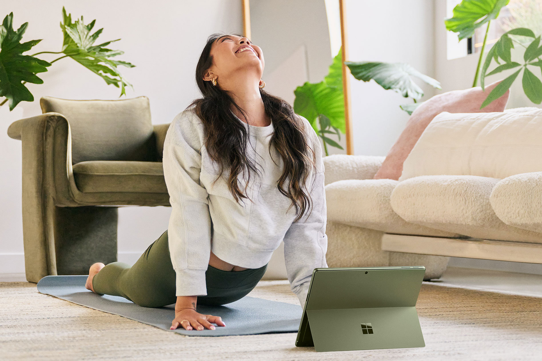 A woman performs a yoga pose on a living room floor with her Surface Pro 9 directly in front of her.