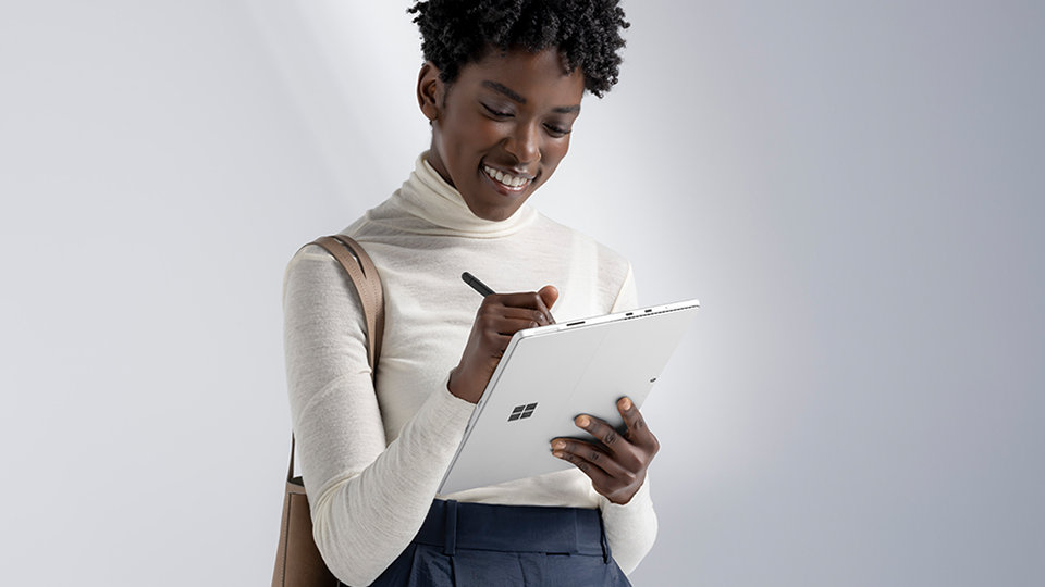 A smiling woman writing with a Slim Pen on a Surface device.