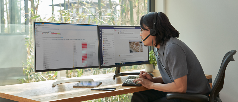 一個人戴著頭戴式耳機在桌上使用雙螢幕工作，螢幕顯示著圖形和電子郵件，