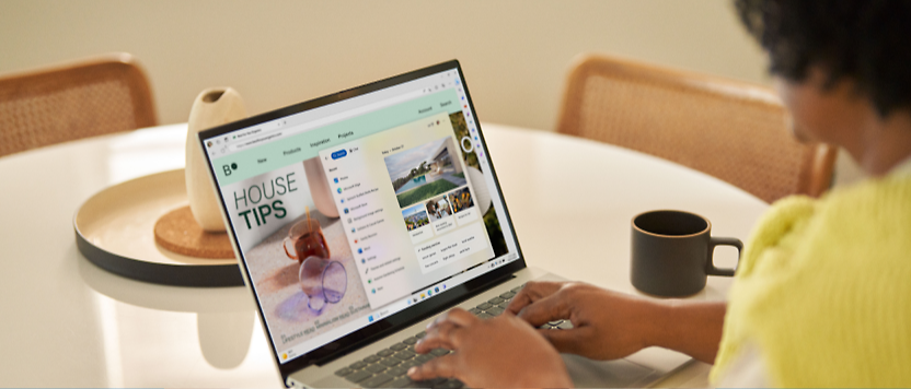 一個人穿黃色上衣在廚房桌上使用膝上型電腦，螢幕顯示一個網站，標題為「房屋提示」