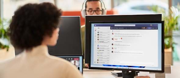 O femeie colaborând în timpul unei întâlniri Microsoft Teams în timp ce lucrează într-un birou deschisă, pe două monitoare