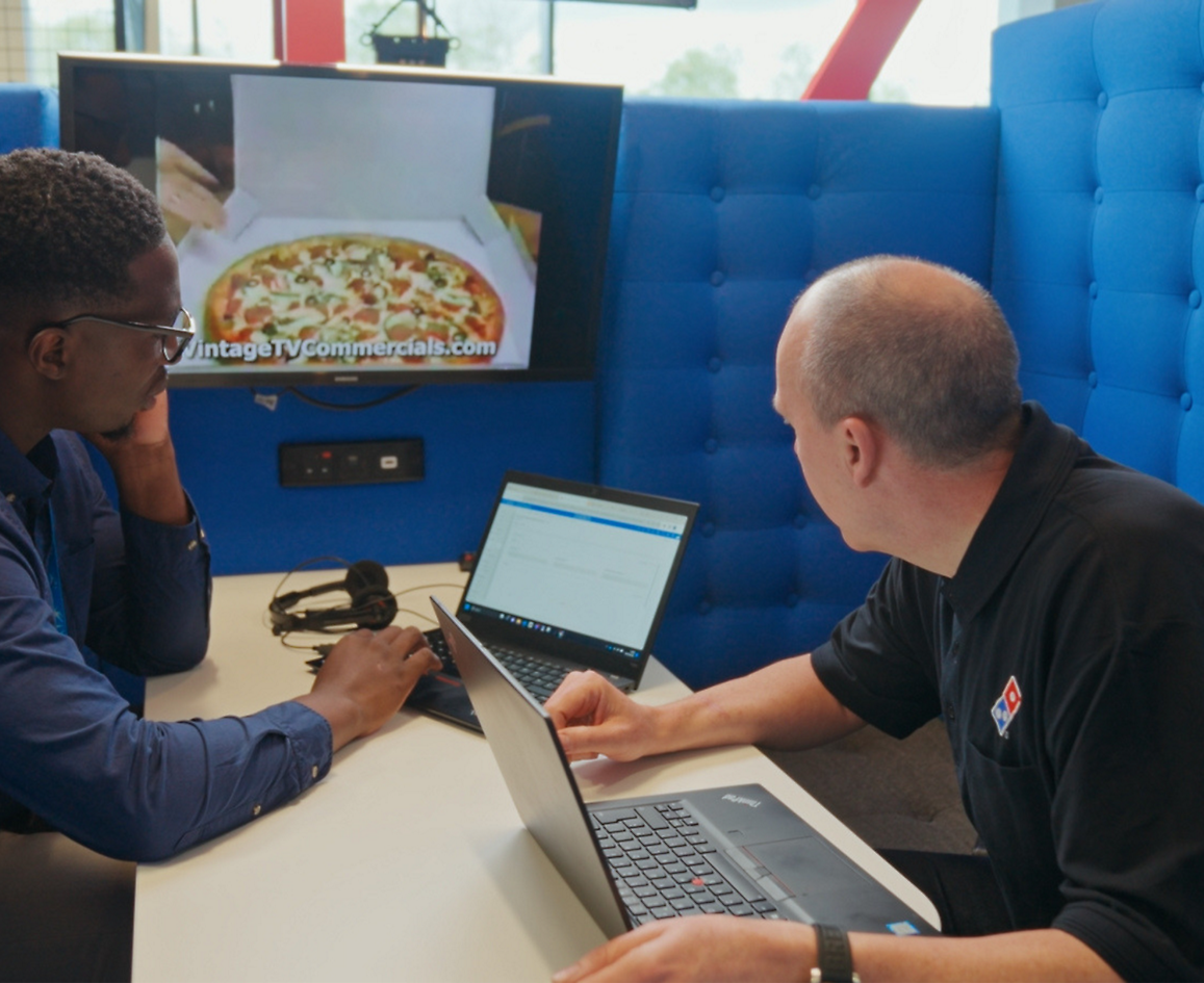 Duas pessoas sentadas com um computador portátil e a falar sobre a Dominos pizza