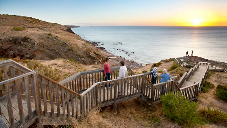 Güney Avustralya'da gün batımında okyanus boyunca tepelere inşa edilmiş ahşap bir tahta üzerinde yürüyen insanlar.