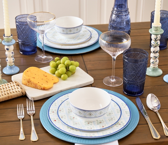 Dining table set with ooh la la blue and white dinnerware, glassware, cheese board, and more.