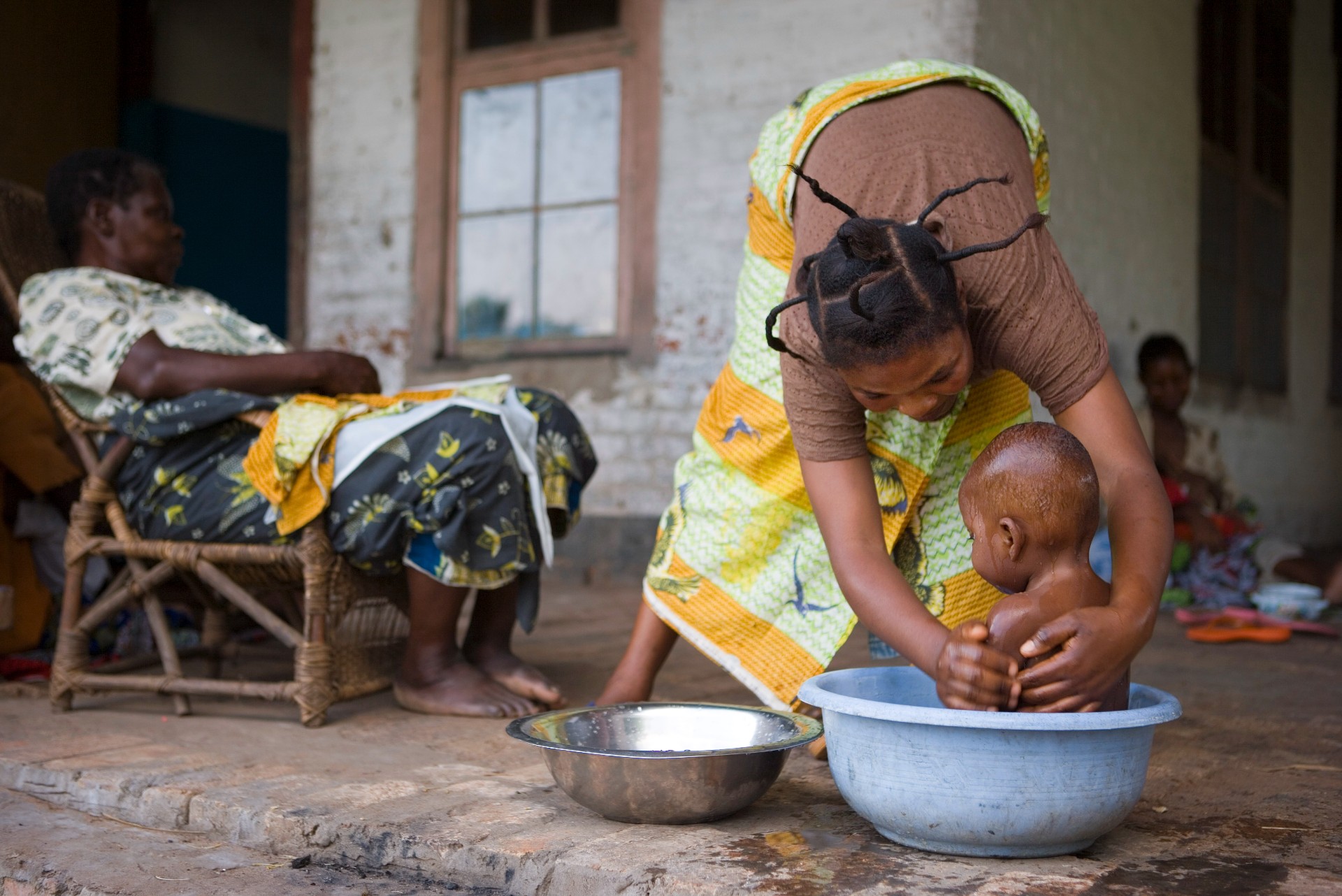 A woman is bathing her child in a bowl.