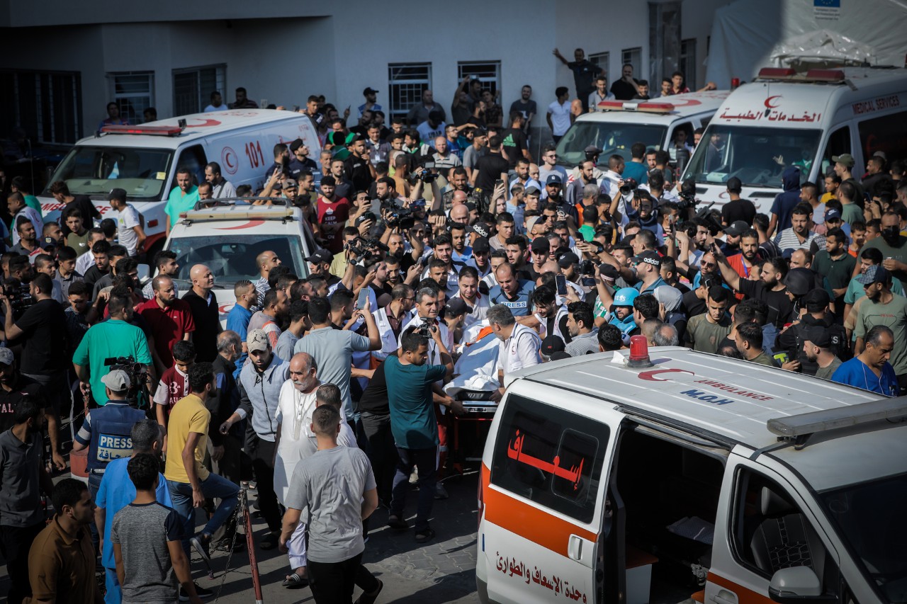 A crowd of people milling around ambulances in a street