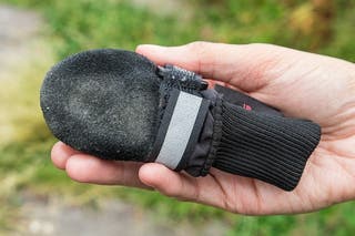 A hand holds up a single Muttluk to show its underside, which is black suede, dusty with wear.