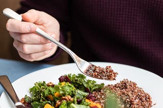 A close image of someone using their flatware "American style" to eat a small salad.