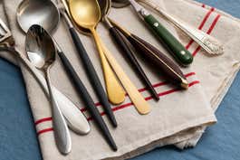 A collection of different types of flatware resting on a tablecloth.