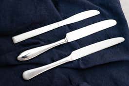 Three examples of different knife styles sitting next to each other on a blue table cloth.
