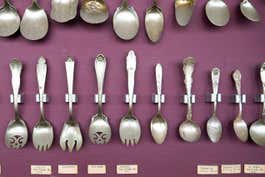 A collection of old spoons mounted on a purple wall.