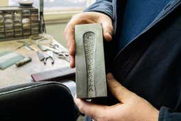 A man holds a metal block that has a recess filled with patterns like you'd see on flatware.