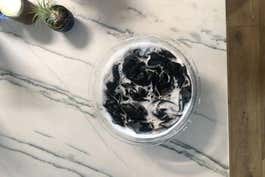 A bowl of black clothes soaking in water on top of a marble counter.