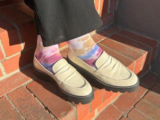 A person wearing multi-colored tie dye socks with white leather loafers.