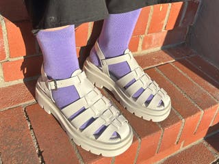A person wearing white monolith sandals with bright purple socks.