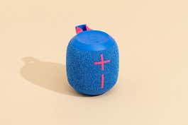 A blue Ultimate Ears Wonderboom 3 bluetooth speaker, in front of a sand-colored background.