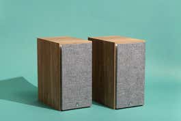 A pair of Triangle Borea BR03 bookshelf speakers, in front of a teal background.