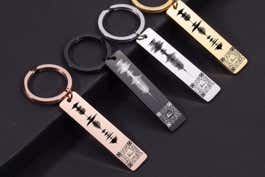 Four different color versions of the Custom Audio Scan QR Code Personalized Keychains, on top of a black surface.