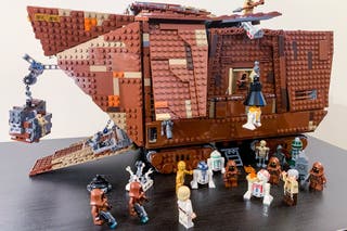 The lego sand crawler vehicle from star wars next to 18 lego characters including droids, jawas, luke and his uncle.