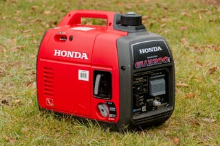 A red Honda EU2200i portable generator outside on a grassy lawn
