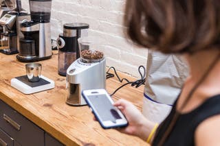 A person holding an iPhone and timing as the Capresso grinder runs on the kitchen counter.