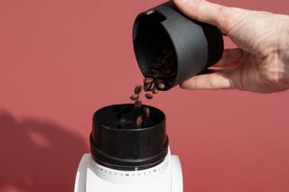 A hand pouring coffee beans into an Encore's single-dose hopper.