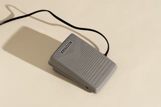 The standard gray foot pedal that is connected by a wire to the Quantum Stylist.
