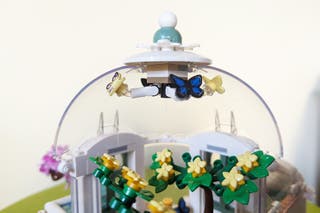 A close-up of a clear plastic dome lego piece with butterflies hanging over yellow lego flowers.