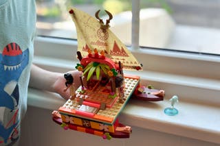A kid playing with Moana’s Wayfinding Boat on a windowsill.