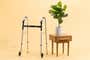 The Drive Deluxe Trigger Release Folding Walker, next to a potted plant in front of a beige background.