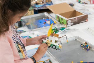 A young girl holds a nearly completed lego camper van. 