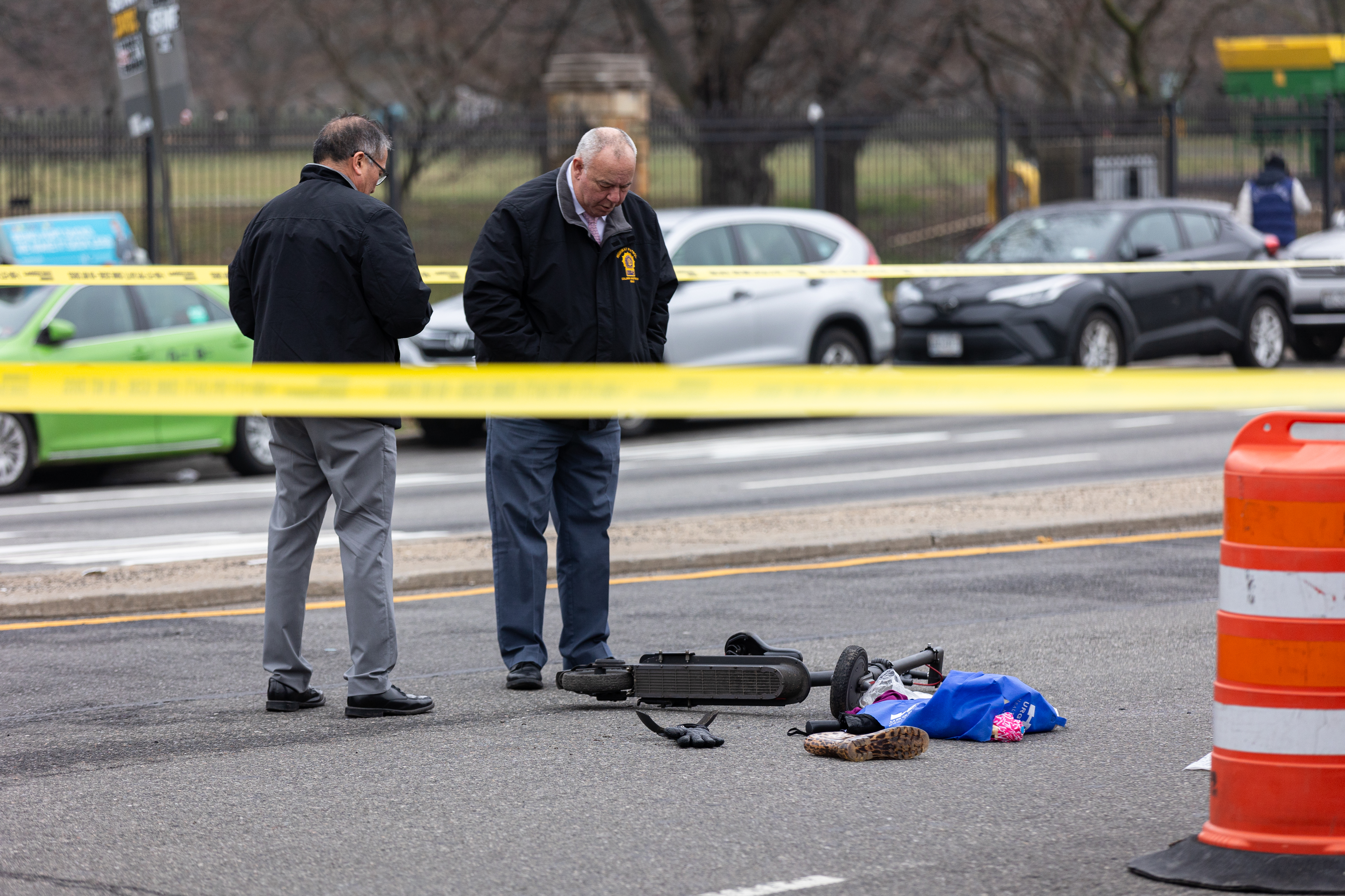 Officers, behind police tape, look at a scooter lying on the road.