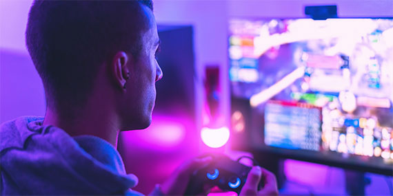 Photograph of man holding game remote playing game on computer screen.  Whole photo has pinkish hue