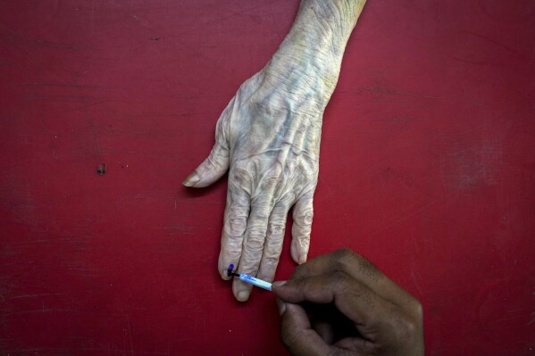 FILE- A polling official puts indelible ink mark on the index finger of 89-year-old Rubi Paul, after she cast her vote at her residence using postal ballot, in Guwahati, India, Sunday, April 28, 2024. (AP Photo/Anupam Nath)