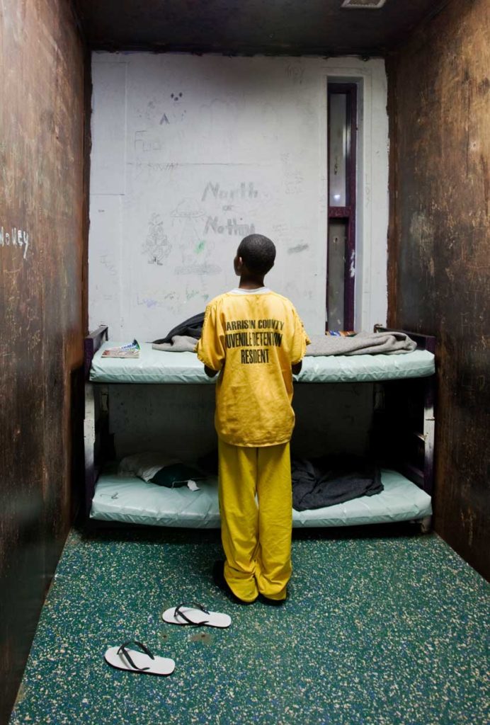 Young Black boy in yellow jumpsuit in detention cell