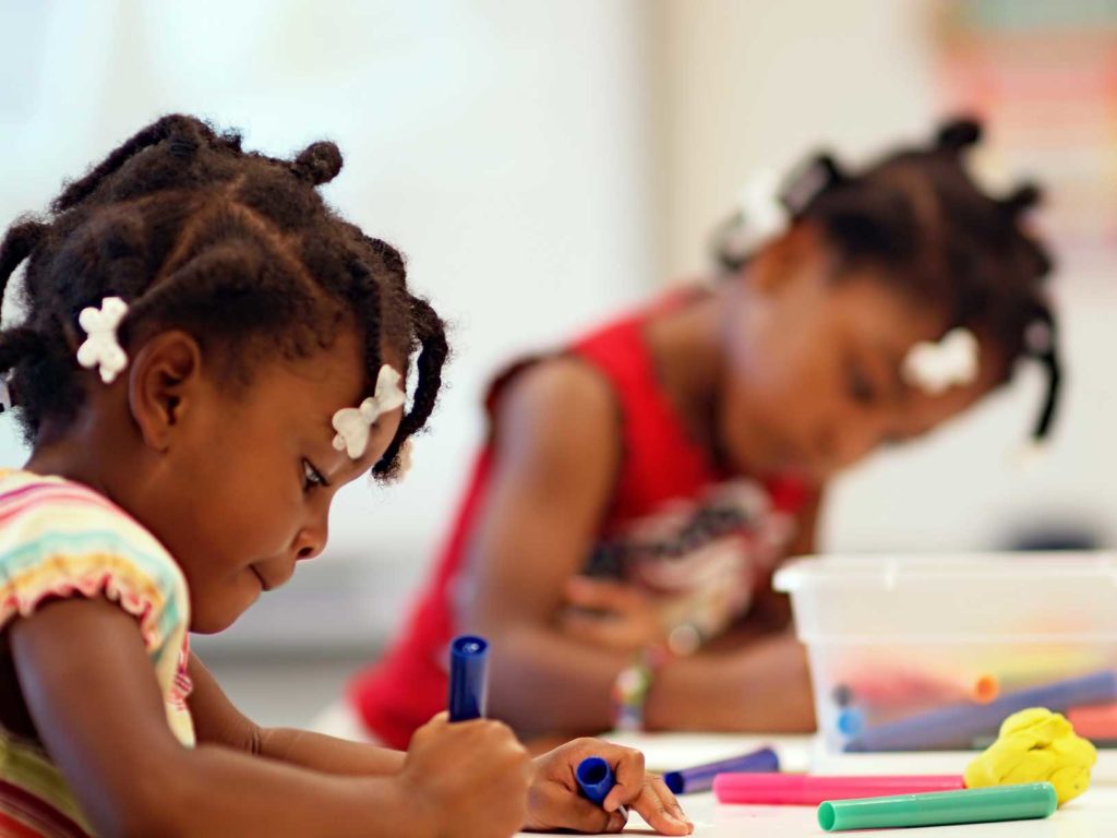 Two young African American girls coloring in school